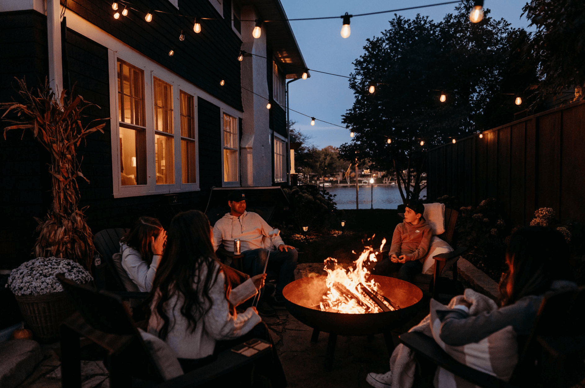 people gathered around a fire pit next to a home.